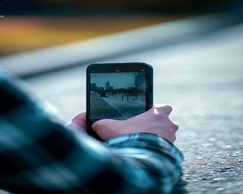 An individual holding a smartphone outdoors with a soft blurred urban environment in the background
