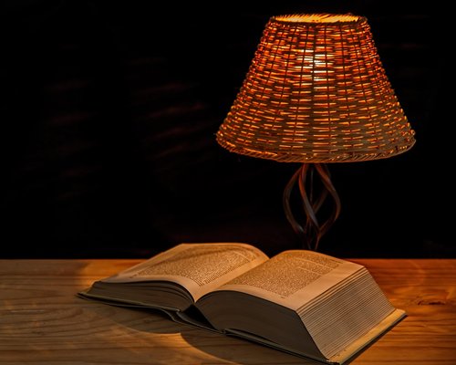 Cozy evening lighting setup with a warm lamp illuminating an open physical book on a nightstand
